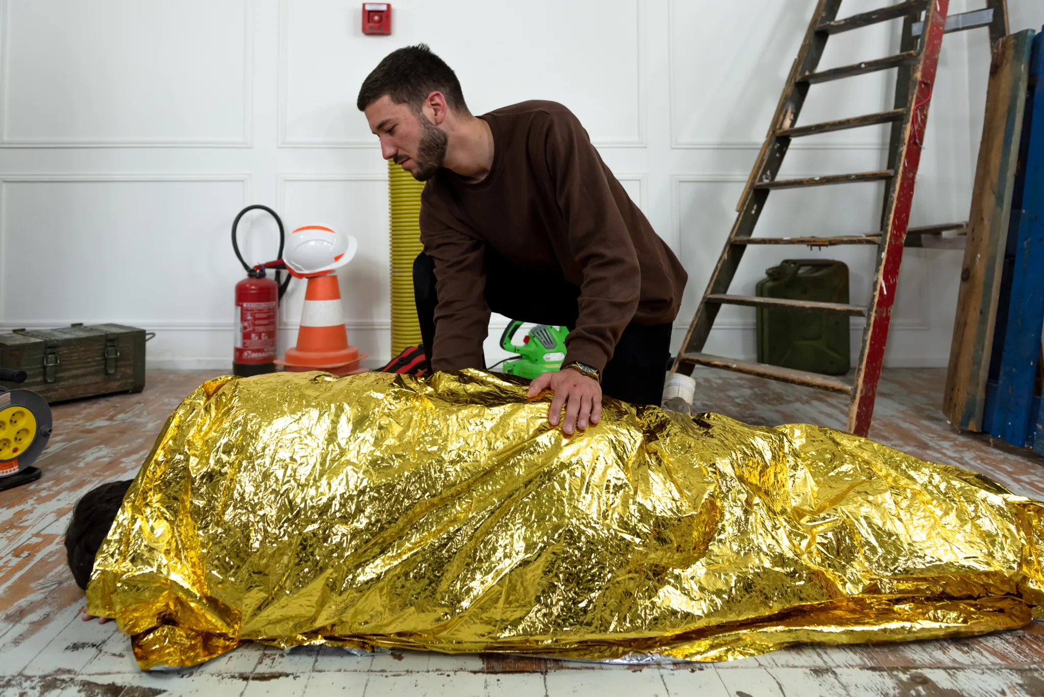 Homme utilisant une couverture de survie sur une personne allongée.